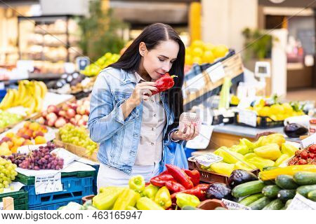 Brunette Wman Smells Red Pepper From Colorful Selection Of Fruit And Vegetables In The Farmers Marke