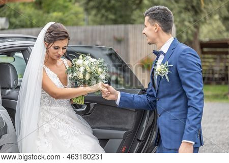 Husband From A Just Married Couple Gives A Heloing Hand To His Wife Getting Out Of The Car.