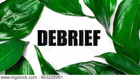 Against The Background Of Green Natural Leaves, A White Card With The Text Debrief