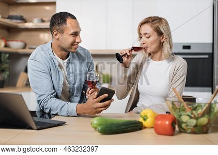 Distracted From Cooking Happy Young Multinational Family Couple Using Cellphone Checking Interesting