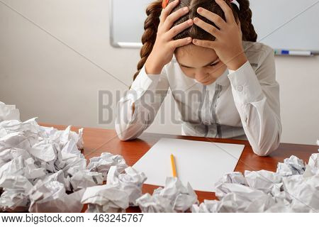 Irritated Young Schoolgirl With Two Pigtails Sitting At The Table With Her Hands Around The Head, Th