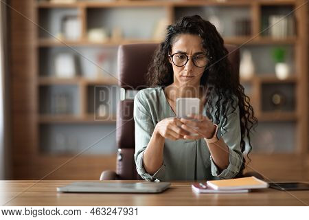 Concentrated Woman Entrepreneur Sitting At Workplace, Using Smartphone