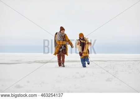 Front View Portrait Of Carefree Young Couple Running Towards Camera Outdoors In Winter By Frozen Lak