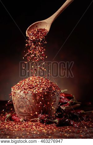 Chilli Flakes Are Poured Into A Wooden Dish. Chilli Flakes And Dried Chili Peppers On A Brown Backgr