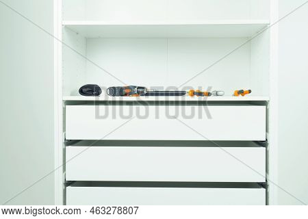 Inserted And Fixed Cabinet Drawers And Shelves. Assembling White Dresser Or Wardrobe. Tools Lie On S