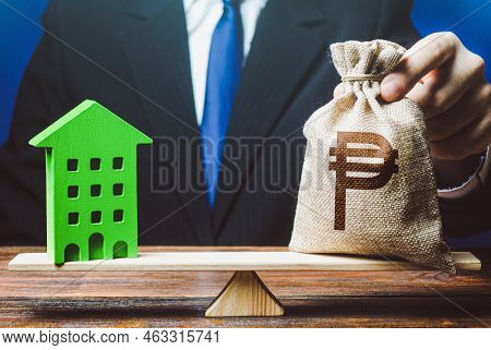 Businessman Puts Philippine Peso Money Bag On Scales And Green House. Investment In Renovation. Prof