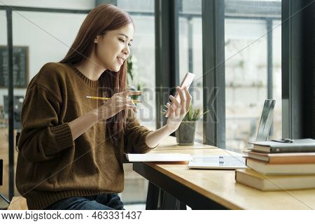 Young Asian Female Student Studying Online Using Laptop And Holding Mobile Phone Surfing The Interne