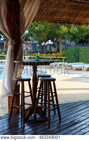 Nobody Seat At The Wooden Stool At The Restaurant Open Air At Noon Near By A Pool. Outdoor Cafe With