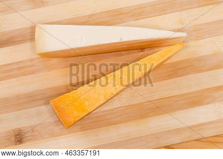 Two Pieces Of Hard And Semi-hard Cheese In The Form Of Segments On A Wooden Bamboo Cutting Board, To