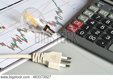 Closeup Of Energy Save Light Bulb, Calculator And Electric Plug Over Printed Graph. Concept For The 