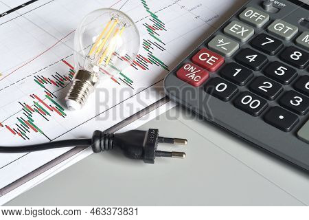 Closeup Of Energy Save Light Bulb, Calculator And Electric Plug Over Printed Graph. Concept For The 