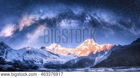 Milky Way Arch Over Snowy Mountains At Starry Night In Winter. Landscape With Snow Covered High Rock