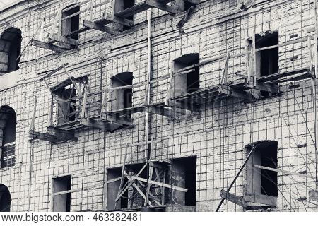 Brick Wall Of Old Destroyed House Without Windows With Wooden Broken Scaffold. Abandoned Repair Of U