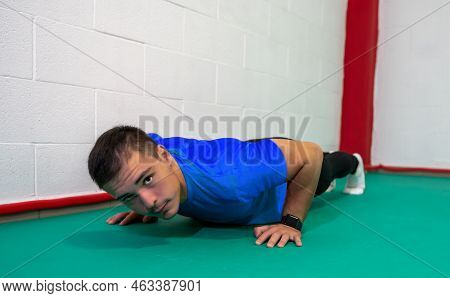 Determined Strong Young Man Doing Push-ups And Looking At Camera. He Is Dressed In An Orange Shirt A