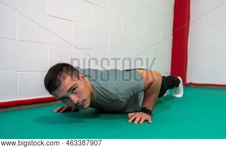 Determined Strong Young Man Doing Push-ups And Looking At Camera. He Is Dressed In An Grey Shirt And