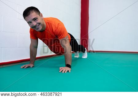 Portrait Of A Strong Determined Young Man Doing Push-ups And Looking At Camera Smiling. He Is Dresse