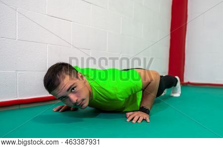 Determined Strong Young Man Doing Push-ups And Looking At Camera. He Is Dressed In An Orange Shirt A