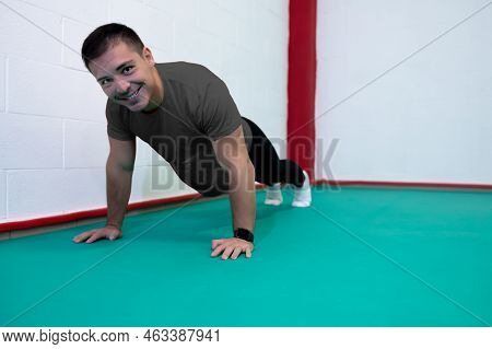 Portrait Of A Strong Determined Young Man Doing Push-ups And Looking At Camera Smiling. He Is Dresse