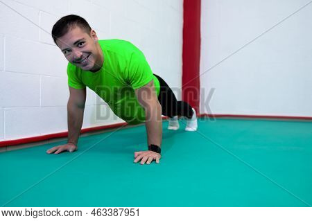 Portrait Of A Strong Determined Young Man Doing Push-ups And Looking At Camera Smiling. He Is Dresse