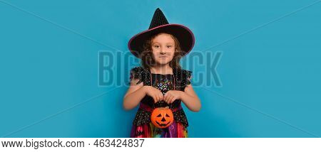 Cute Little Girl In Halloween Witch Dress Or Wizard Costume Holding Pumpkin Candy Basket Or Jack O L