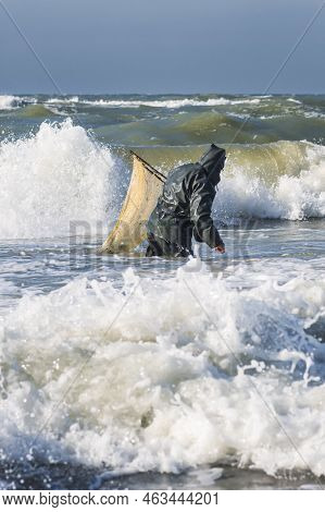 Amber Catching In The Baltic Sea. Amber Catcher Or Fisherman With Fisherman\'s Coat And Boots Into T