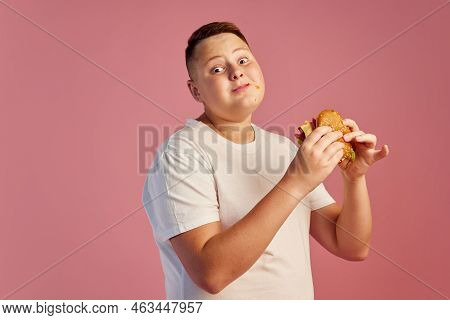 Half-length Portrait Of Cute Overweight Boy In White T-shirt Tasting Delicious Burger Isolated On Pi