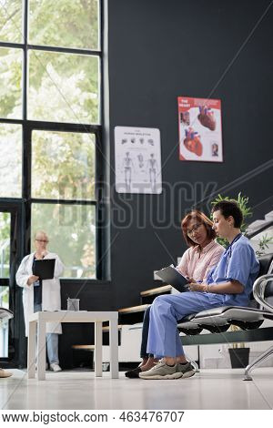Medical Asisstant Consulting Senior Patient In Hospital Waiting Area, Filling Report Papers Explaini