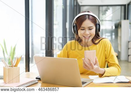Young Asian Female Student Studying Online Using Laptop And Holding Mobile Phone Surfing The Interne