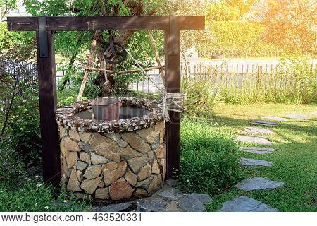 Beautiful Artesian Well Made By Stones And Wheel Pulley With Metal Bucket And Rope In Peaceful Garde