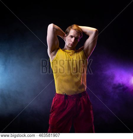A Young Muscular Man In A Bright Outfit Poses In A Pretentious Pose, Style And Grotesque. Attractive