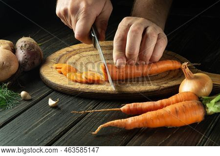 The Chef Cuts Fresh Carots On A Wooden Cutting Board. Close-up Of Cook Hands While Preparing Vegetar