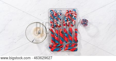 Flat Lay. Drizzling White Glaze On Top Of Patriotic Cinnamon Twists. And Decorating With Star Sprink