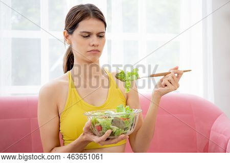 Young Caucasian Woman Sitting On Sofa Eating Vegetable Salad While Feeling Dislike And Expression Di