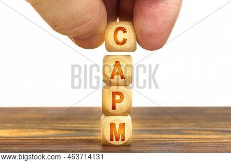 Business Concept. A Man Puts Wooden Cubes On The Table With The Inscription - Capm