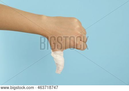 Woman Showing Thumb Down Wrapped In Medical Bandage On Light Blue Background, Closeup