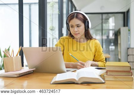 Young Asian Female Student Studying Online Using Laptop And Holding Mobile Phone Surfing The Interne