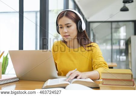 Young Asian Female Student Studying Online Using Laptop And Holding Mobile Phone Surfing The Interne