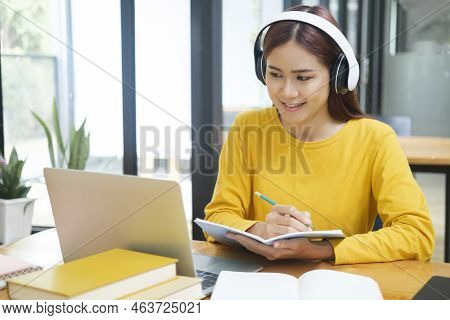 Young Asian Female Student Studying Online Using Laptop And Holding Mobile Phone Surfing The Interne