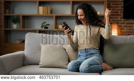 Happy Woman Lady Using Phone For Bet In Internet Receive Message With Good News Offer Sitting On Cou