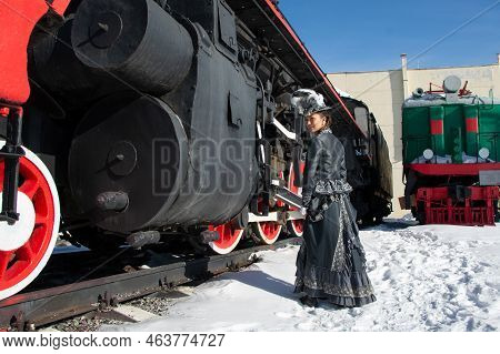 Girl Dressed As A Noblewoman Of The 19Th Century Near A Steam Locomotive. Russian Winter