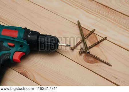 Table With Tool. Electric Screwdriver On A Wooden Table. Side View Of The Black Metallic Screws, Ele