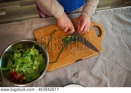 Top View. Details : Womans Hands Using Kitchen Knife, Chopping Young Green Onion On Wooden Cutting B