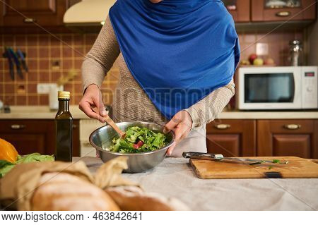 Close-up Housewife Woman In Blue Hijab, Using A Wooden Spoon, Mixes Fresh Ingredients While Cooking 