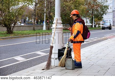 Moscow, Russia - October 2022: Asian Woman Janitor Standing With Smartphone In Autumn City. Rest Dur