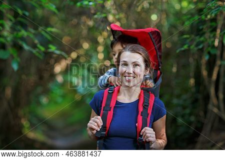 Mother With Toddler Child In Backpack Carrier Is Hiking In Forest. Tourist Is Carrying A Baby On His