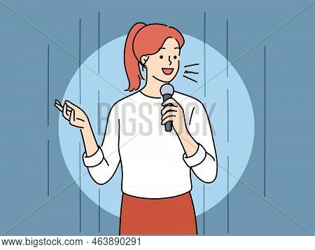 Young Woman With Microphone Performing On Stage. Smiling Female Hold Mic Speak In Front Of Audience.