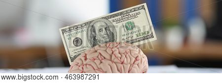 Close-up Of Banknote Put In Anatomical Model Of Human Brain, Mess Of Business Papers On Desk. Make M