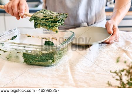 Woman's Hands Putting One Porzione Of Homemade Lasagna With Spinach And Ricotta In A Plate From Glas