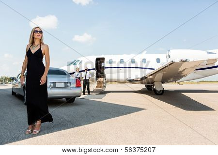 Full length of rich woman in elegant dress standing against limousine and private