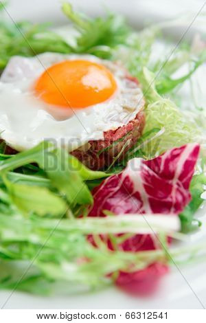 Beef tartar with fried egg and lettuce, close-up